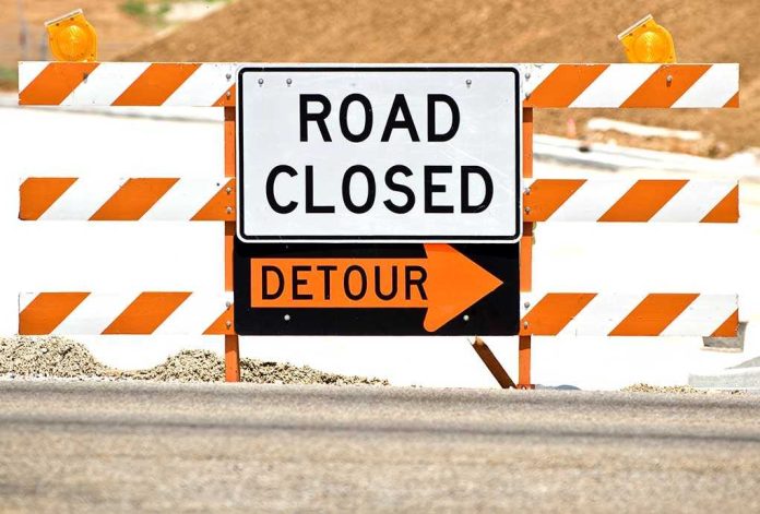 A road closed sign with a detour arrow pointing right